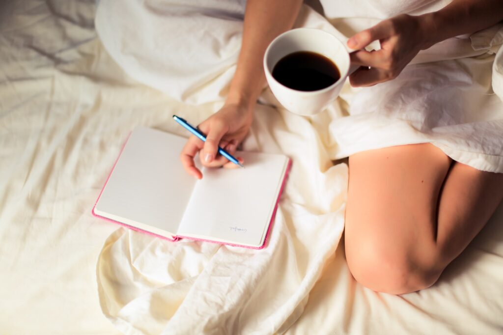 woman drinking coffee making lists in bed