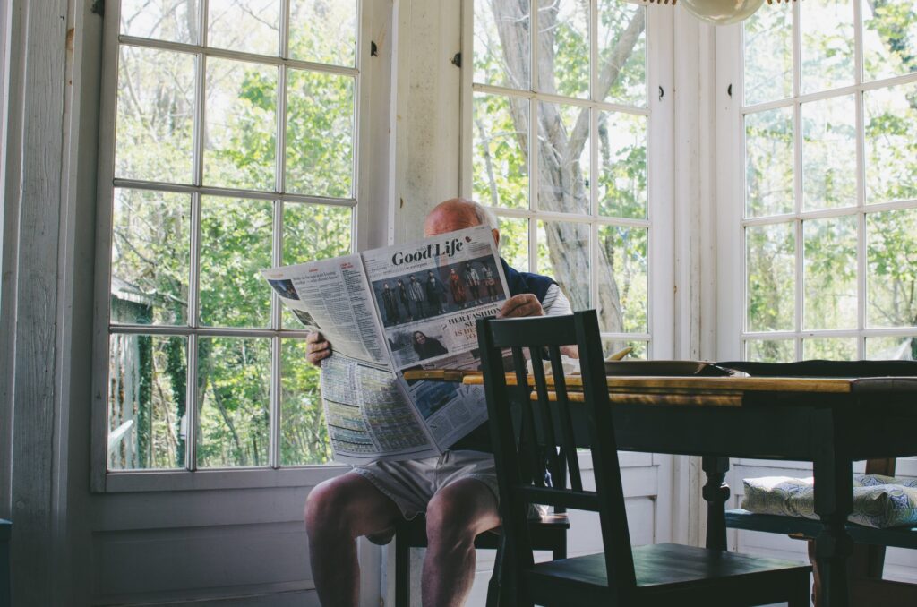 old man sitting in kitchen reading newspaper