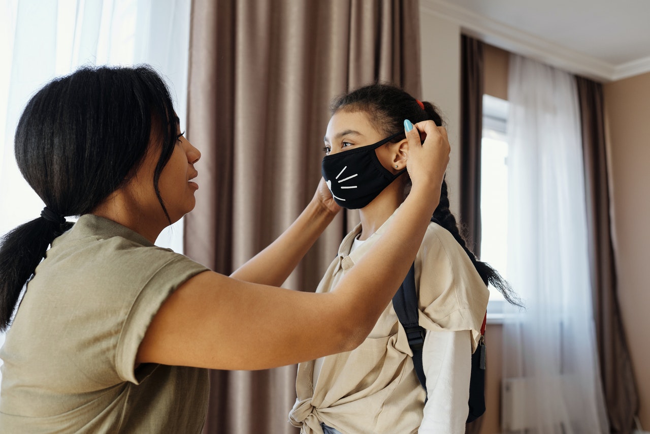 woman putting a face mask on her daughter coronavirus protection