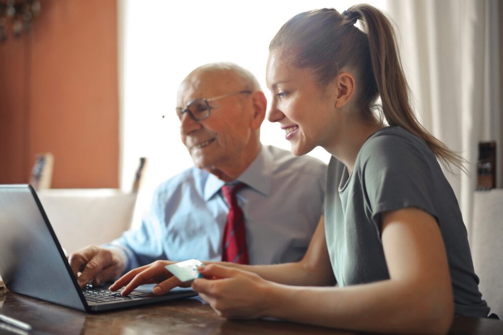 young woman helping old man with laptop