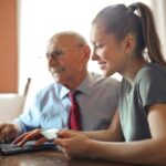 young woman helping old man with laptop