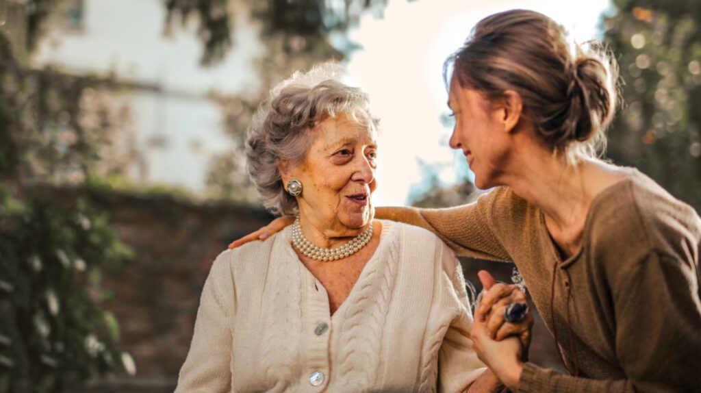 adult daughter holding aging mother's hand smiling