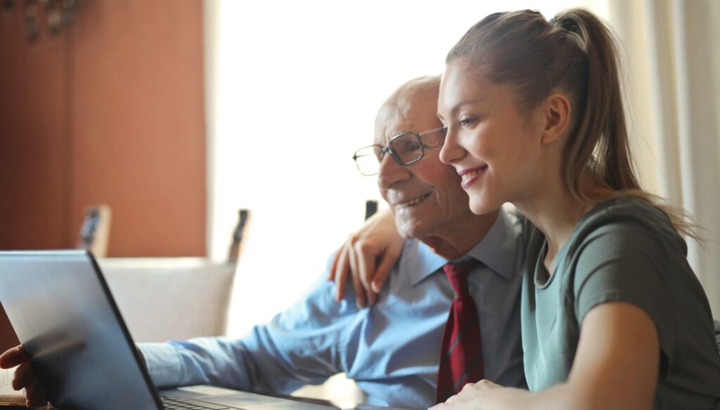 young woman helping aging man on laptop smiling