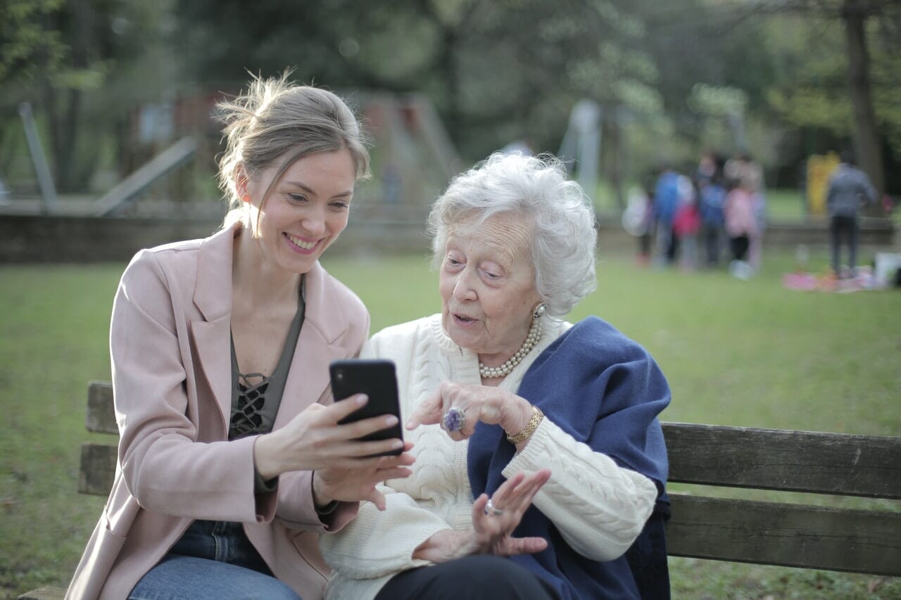 Smiling young woman shows elderly mother pictures on her smartphone