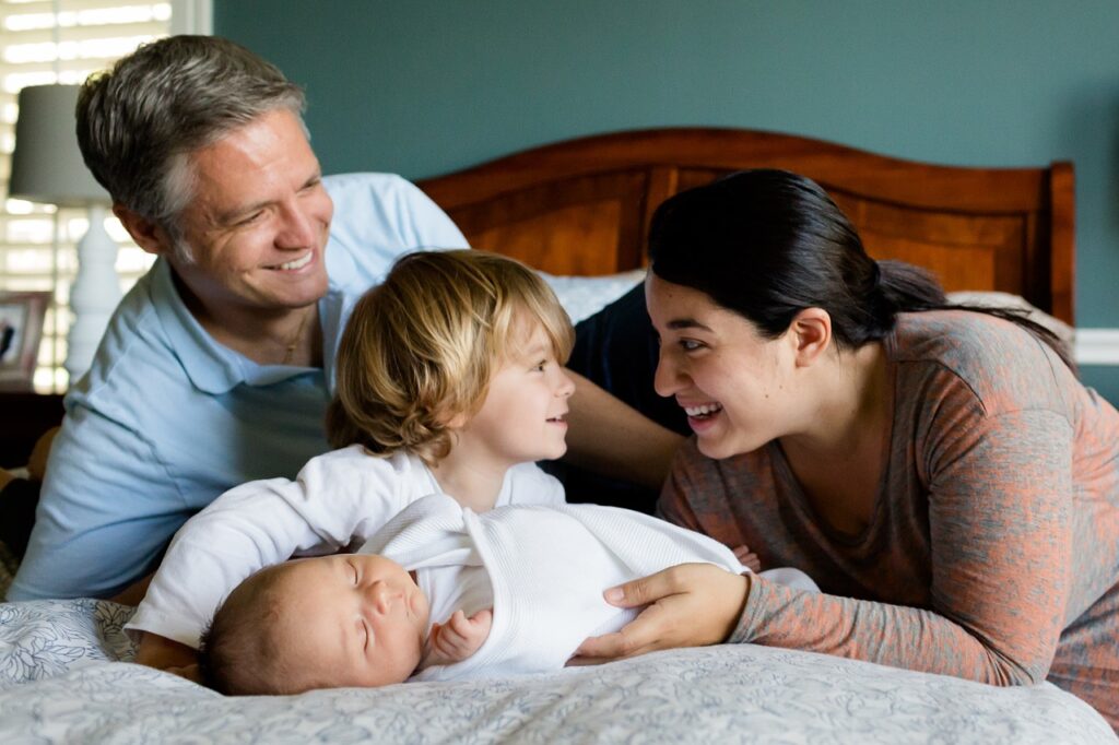 family with toddler and infant posing together on parents bed