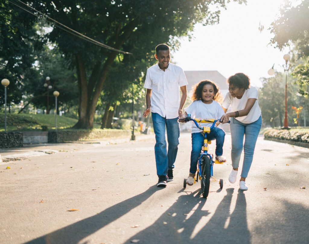 parents teaching young girl to ride a bike on residential street