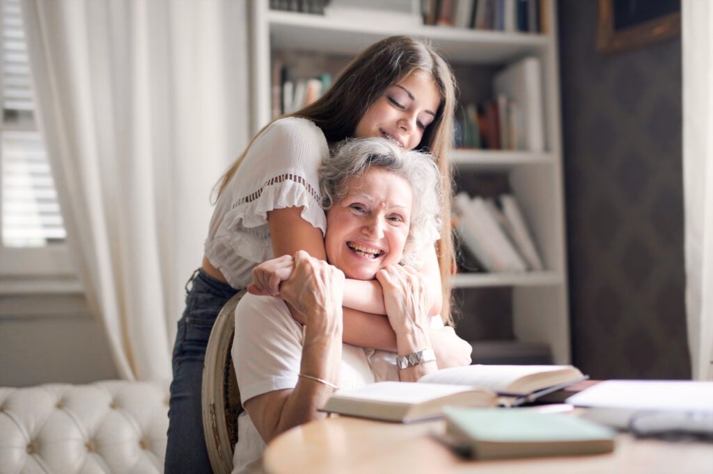 smiling girl hugging smiling grandma from behind