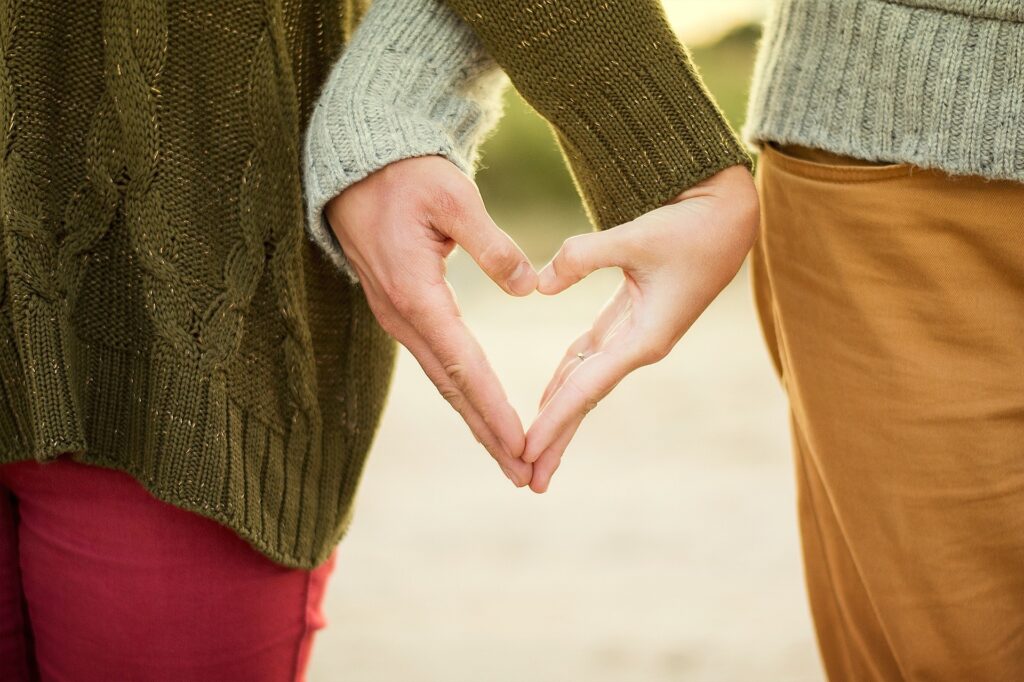 couple standing side by side making heart shape with hands