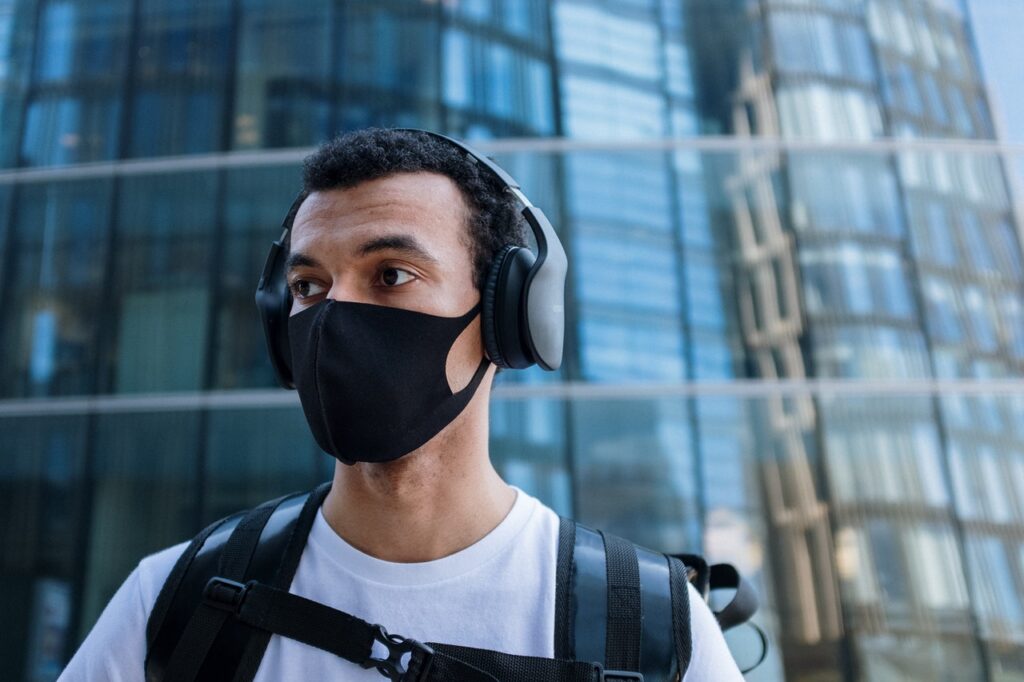 young man wearing masks and headphones in front of glass building