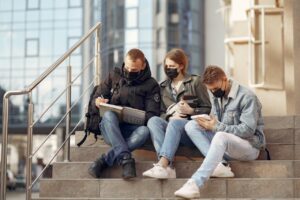 three college students in masks sitting on school steps