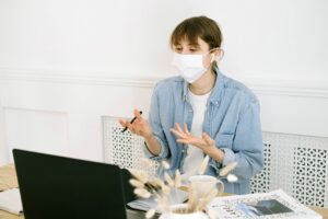woman in mask and denim shirt talking on laptop