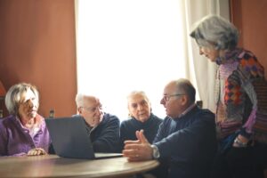 group of older adults conversing around a laptop