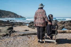 Woman Standing Beside Woman on White Wooden Chair Facing Body of Water