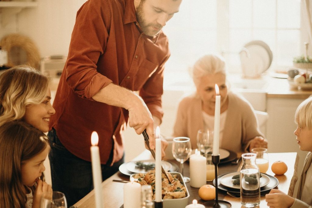 man carving thanksgiving turkey while family looks on