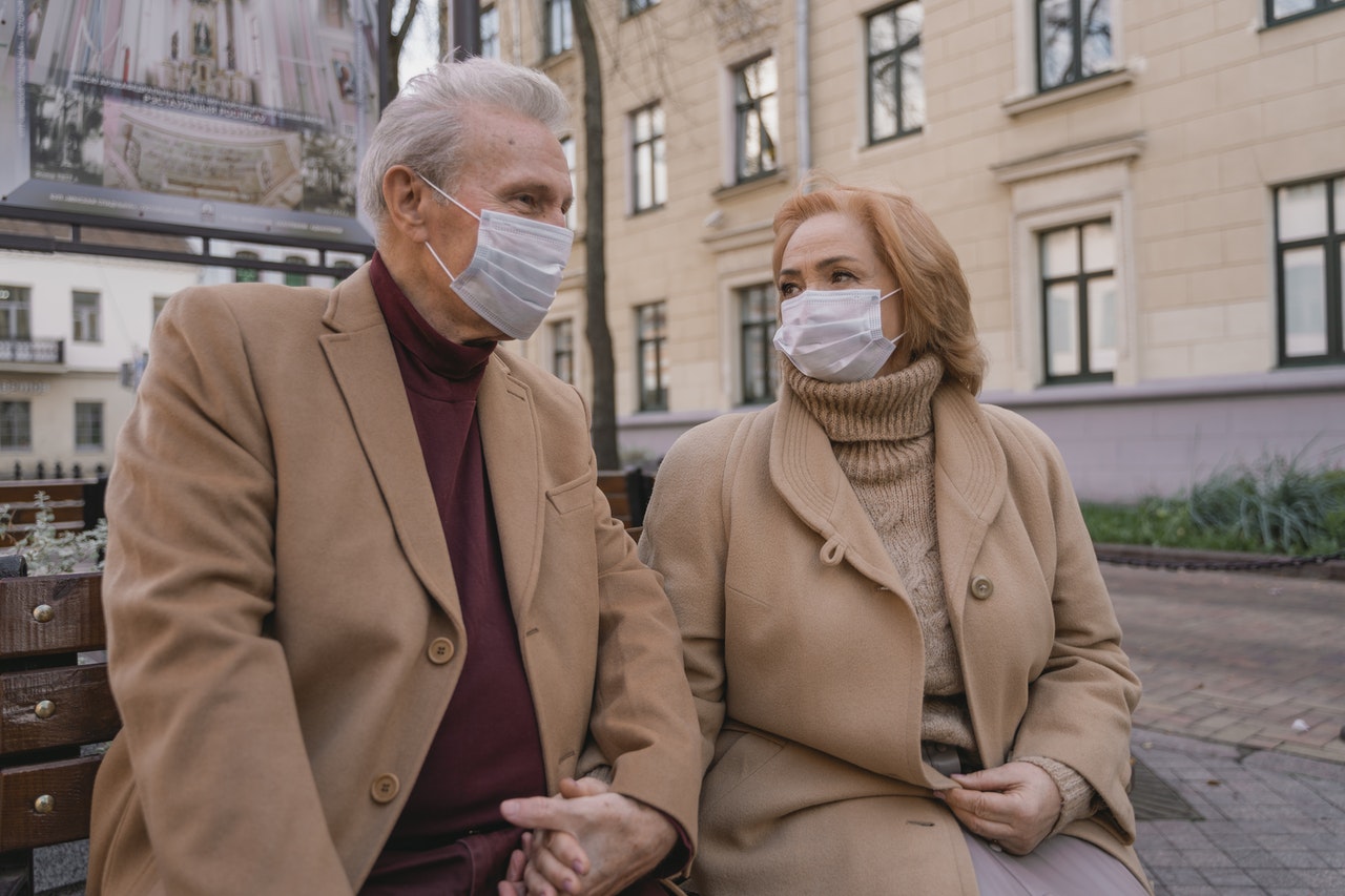 older couple in masks holding hands on a park bench