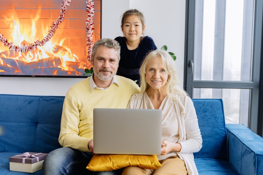 man in yellow shirt and woman in white shirt with laptop and grand daughter looking over their shoulders