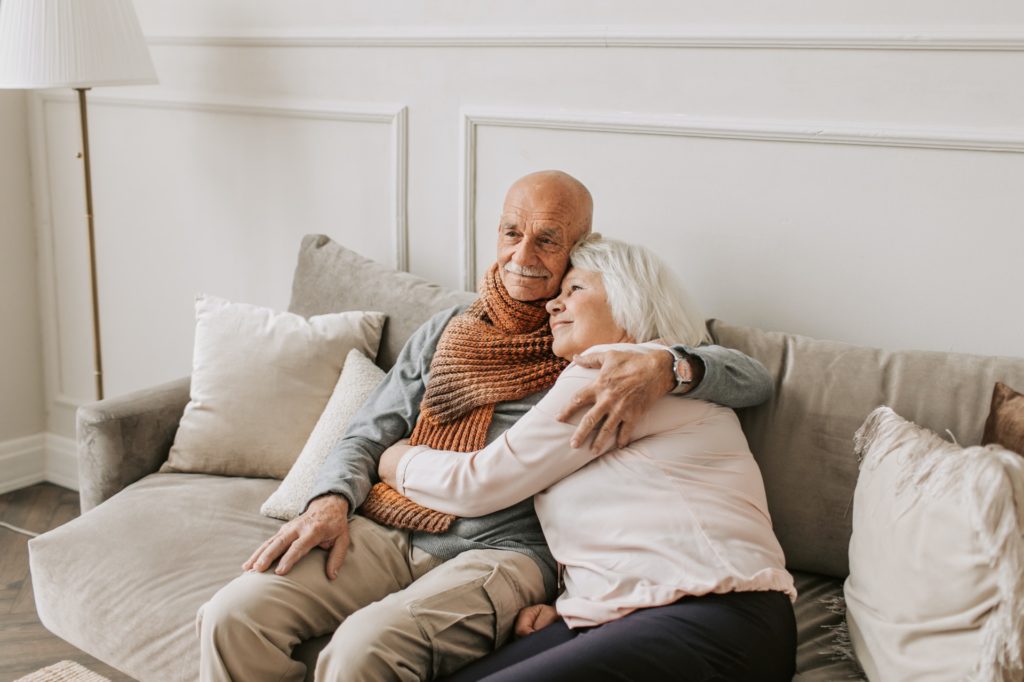 elderly couple sitting on a couch holding each other and smiling