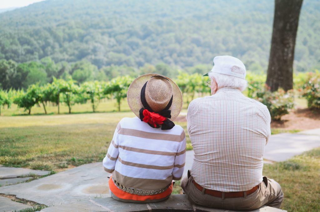 Old couple sitting on a bench looking at a view of trees and hills.