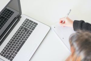 woman writing on notebook next to laptop
