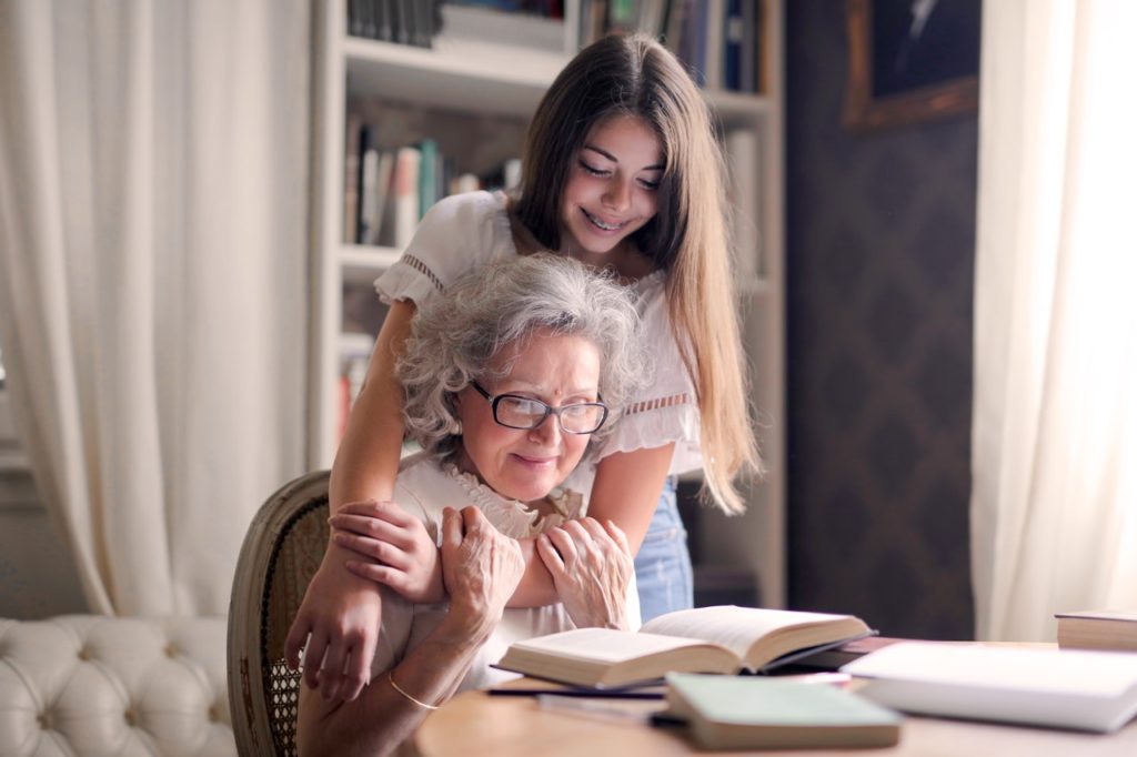 young girl hugs grandma from behind as they look at a book