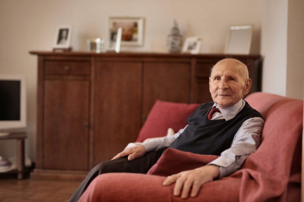 elderly man in a black sweater vest sitting on red sofa