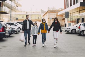 young family in medical masks walking along parking area