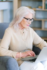 aged woman in eye glasses surfing internet on laptop