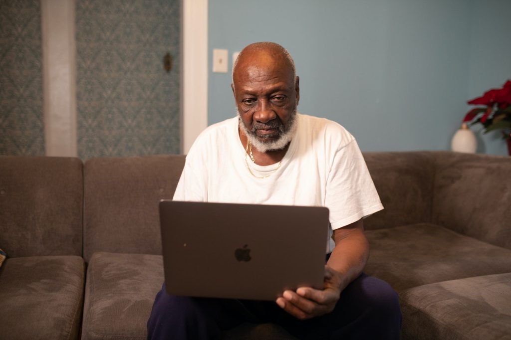 man wearing white crew neck t-shirt sitting while using macbook pro