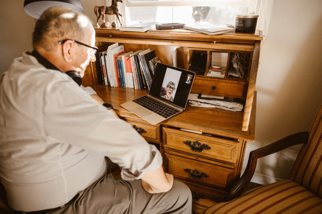old man sitting at a wood desk having a video call with elderly woman