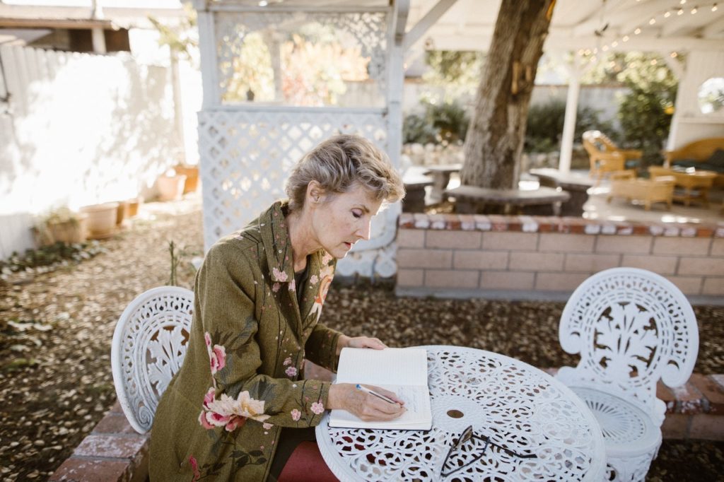 older woman sitting on patio furniture writing in notebook