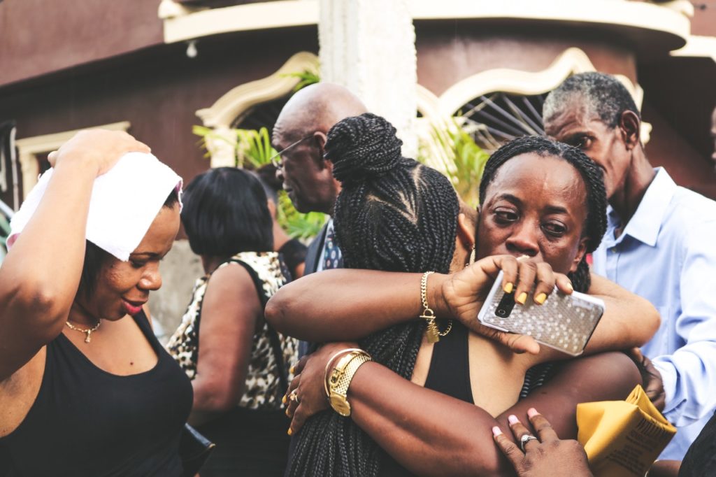 upset black woman embracing another woman near group of people