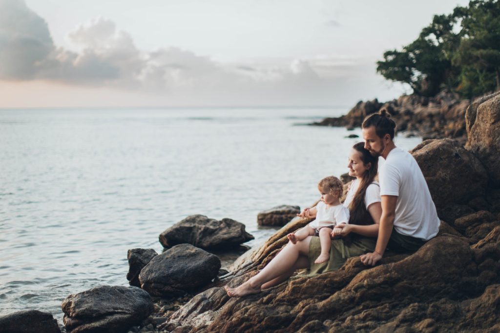 young family with baby sitting by the rocks seaside