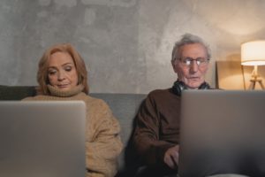 elderly man and woman sitting on couch using laptops