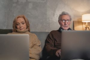 elderly man and woman sitting on couch using laptops