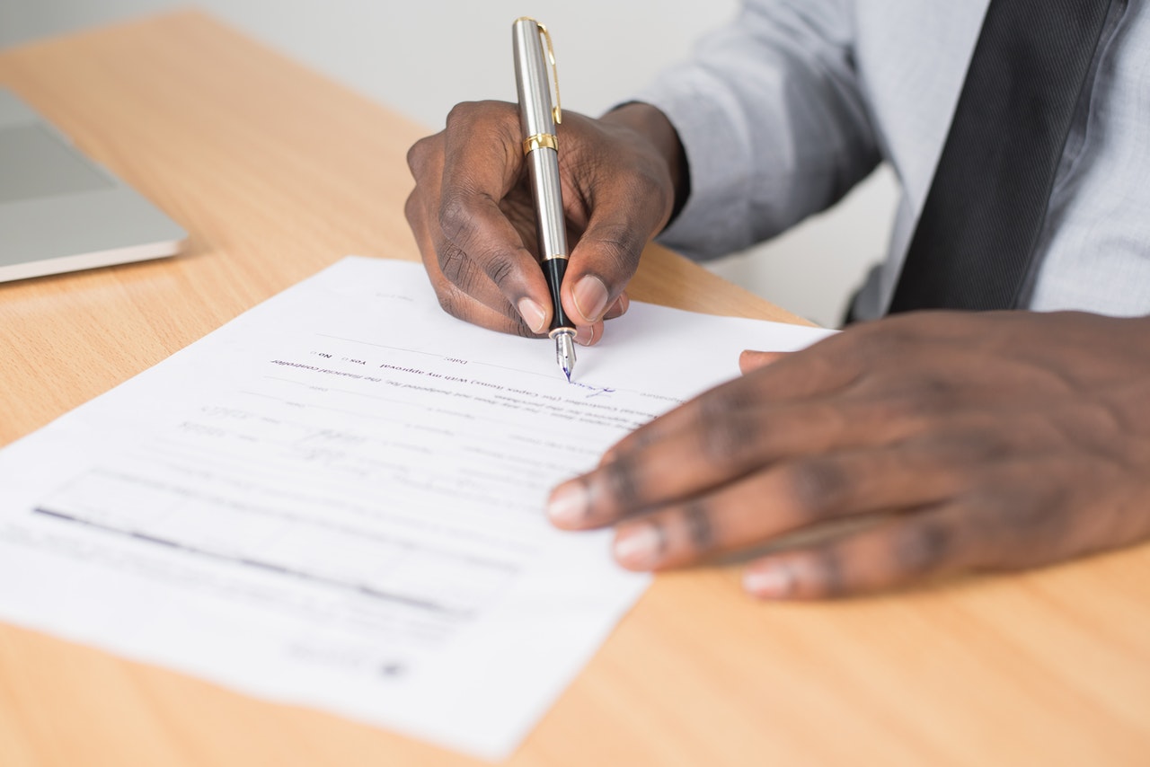 black man holding gray twist pen and white printer paper on brown wooden table