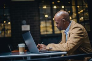 black businessman writing on paper near laptop in cafe