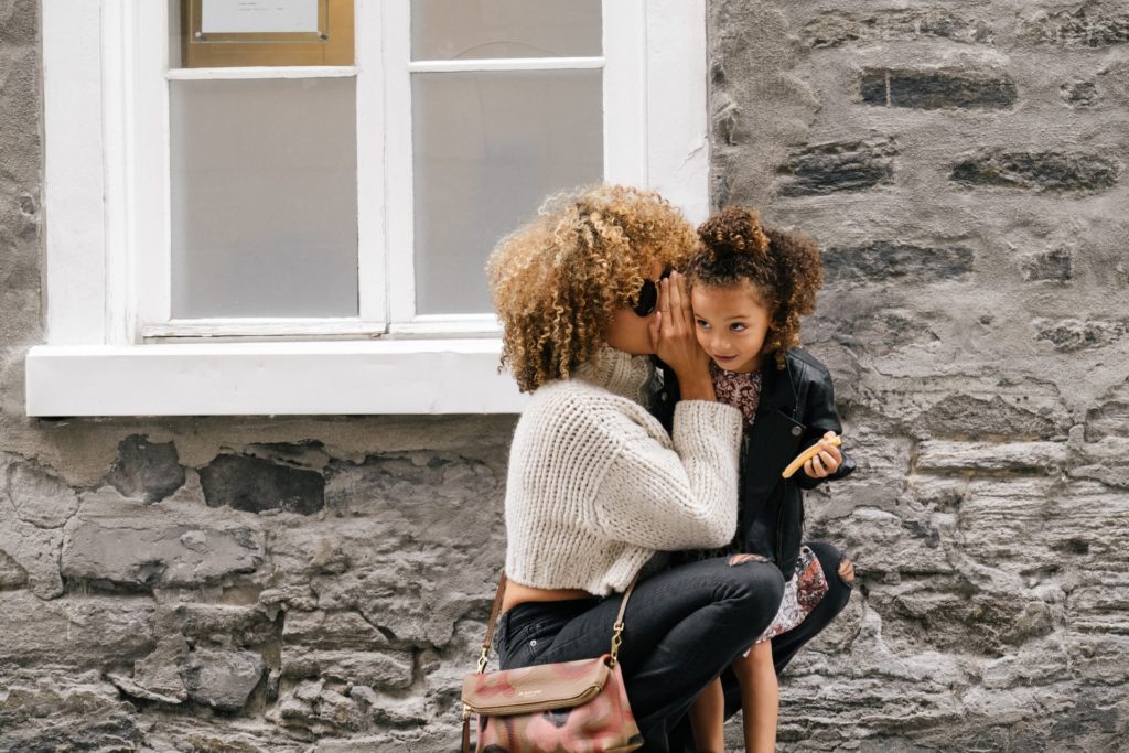 photo of woman kneeling and whispering in her young daughter's ear