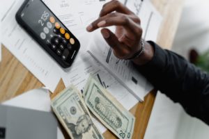 person counting cash with a calculator on a cluttered desk