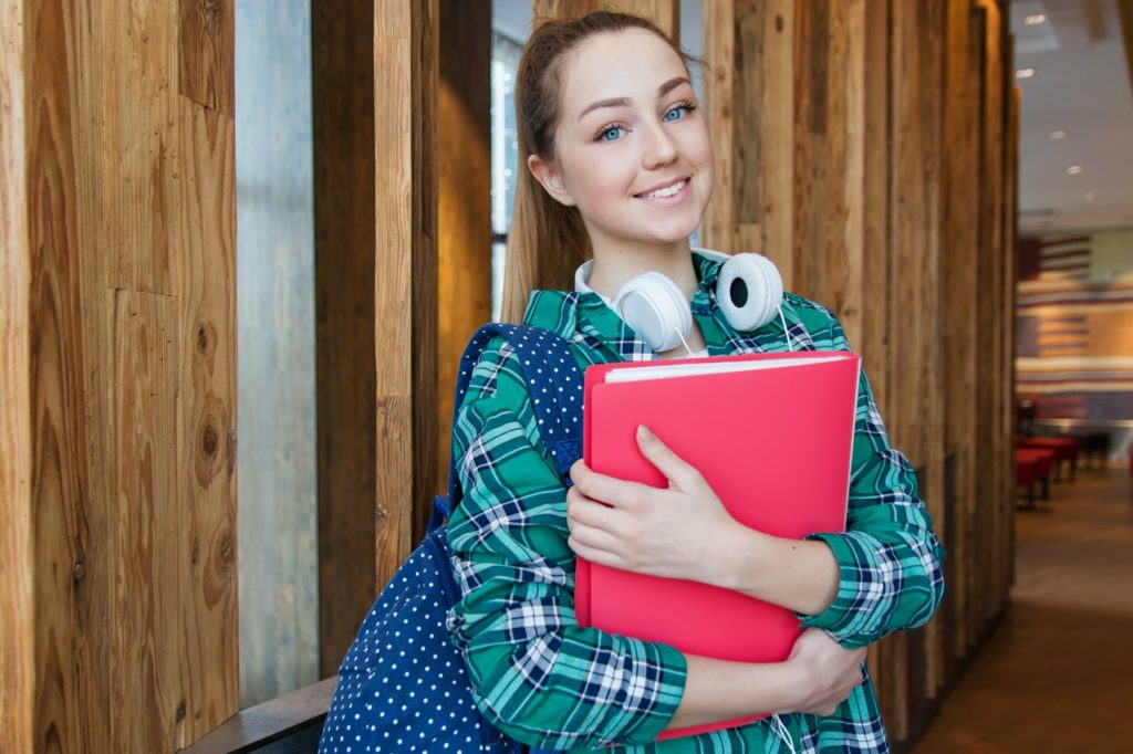 young college woman smiling at camera holding books