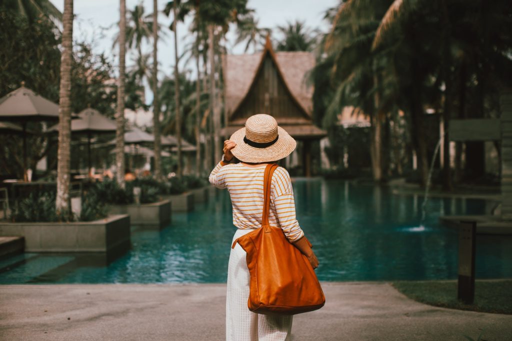 woman in straw hat standing in front of exotic pool resort