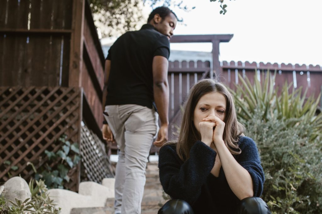 man walking away from woman as she sits on steps in back yard