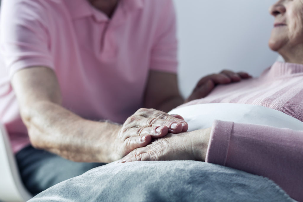 man in pink shirt holding hands with woman in hospital bed