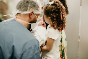 man holds baby so young girl can see