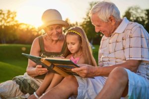 grandparents seated with little girl on grass with scrapbook