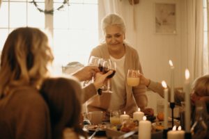older woman smiles down at table as family members raise glasses to cheers