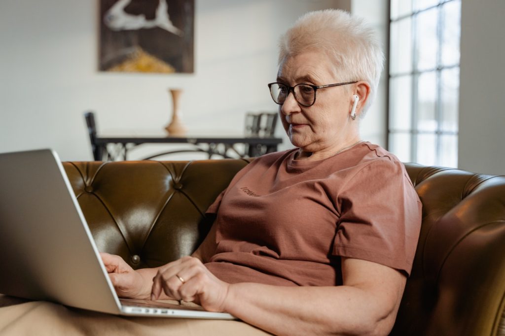 older woman with earbuds on laptop in living room