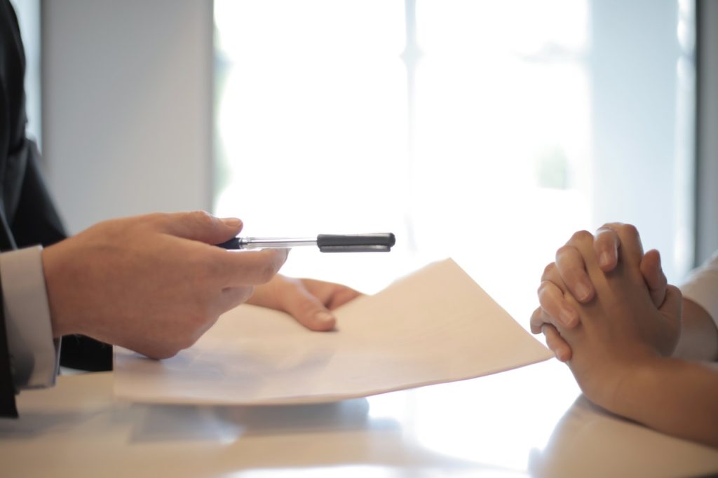 person handing a pen and document across a table for a second person to sign