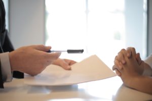 person handing a pen and document across a table for a second person to sign