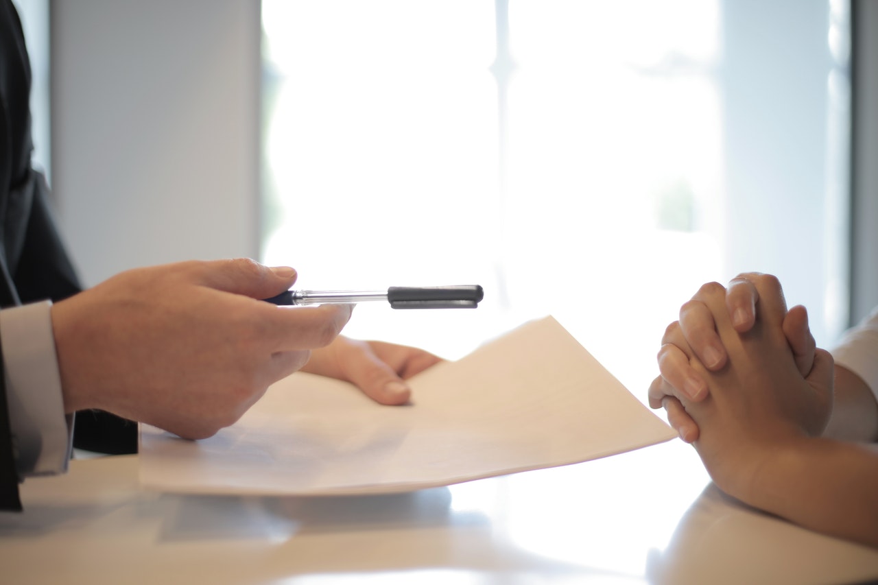 person handing a pen and document across a table for a second person to sign