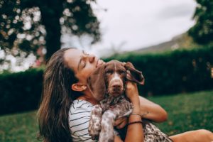 woman cuddles pet dog on her lap while sitting out in a grassy backyard